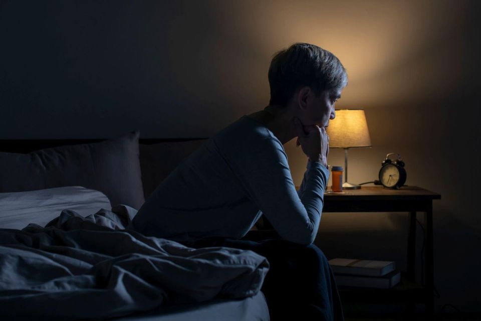 Piekeren en spanning rond het slapengaan Vermoeide persoon zit op de rand van het bed en denkt na over de komende nacht